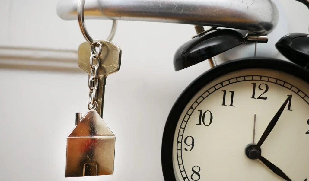 House-shaped keychain hanging near alarm clock symbolizing property investment and time management
